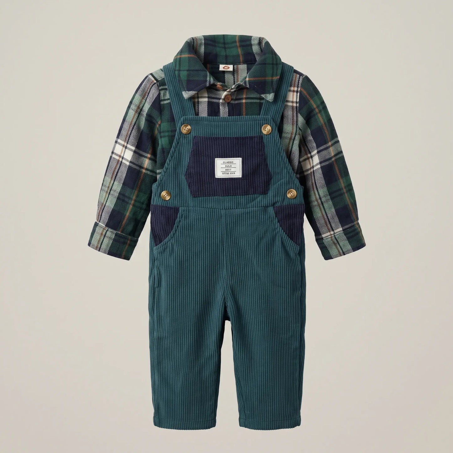 Toddler boy's corduroy overall romper in teal green, styled with a navy and green plaid long-sleeve shirt underneath. The overall features a dark navy bib panel, gold-tone snap buttons, and a white brand label on the chest pocket.