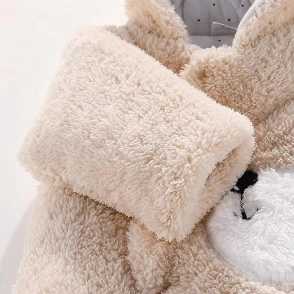 Close-up of a plush teddy bear costume or jacket in cream and white faux fur, showing the soft texture and part of the black embroidered face.