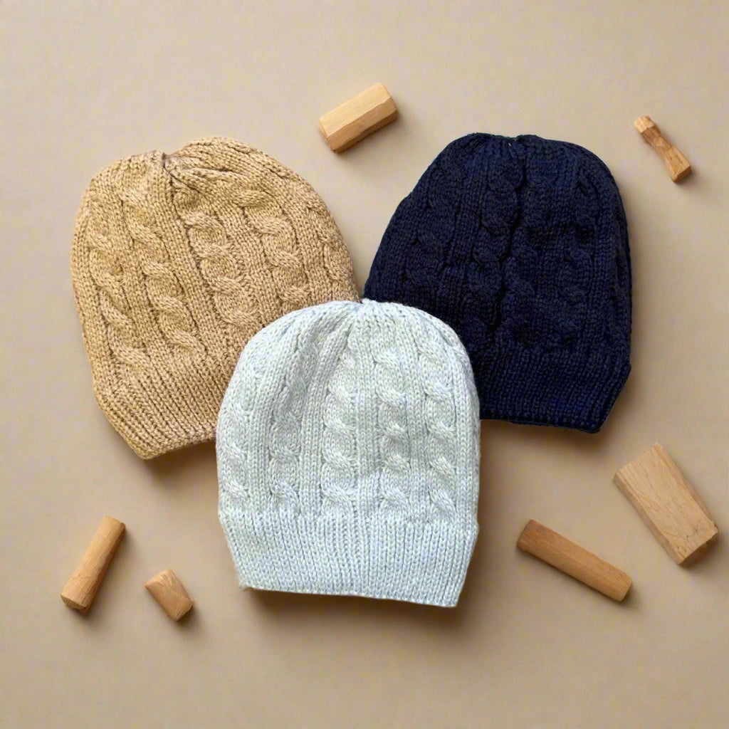 Three knit beanie hats in beige, gray, and navy on a white background