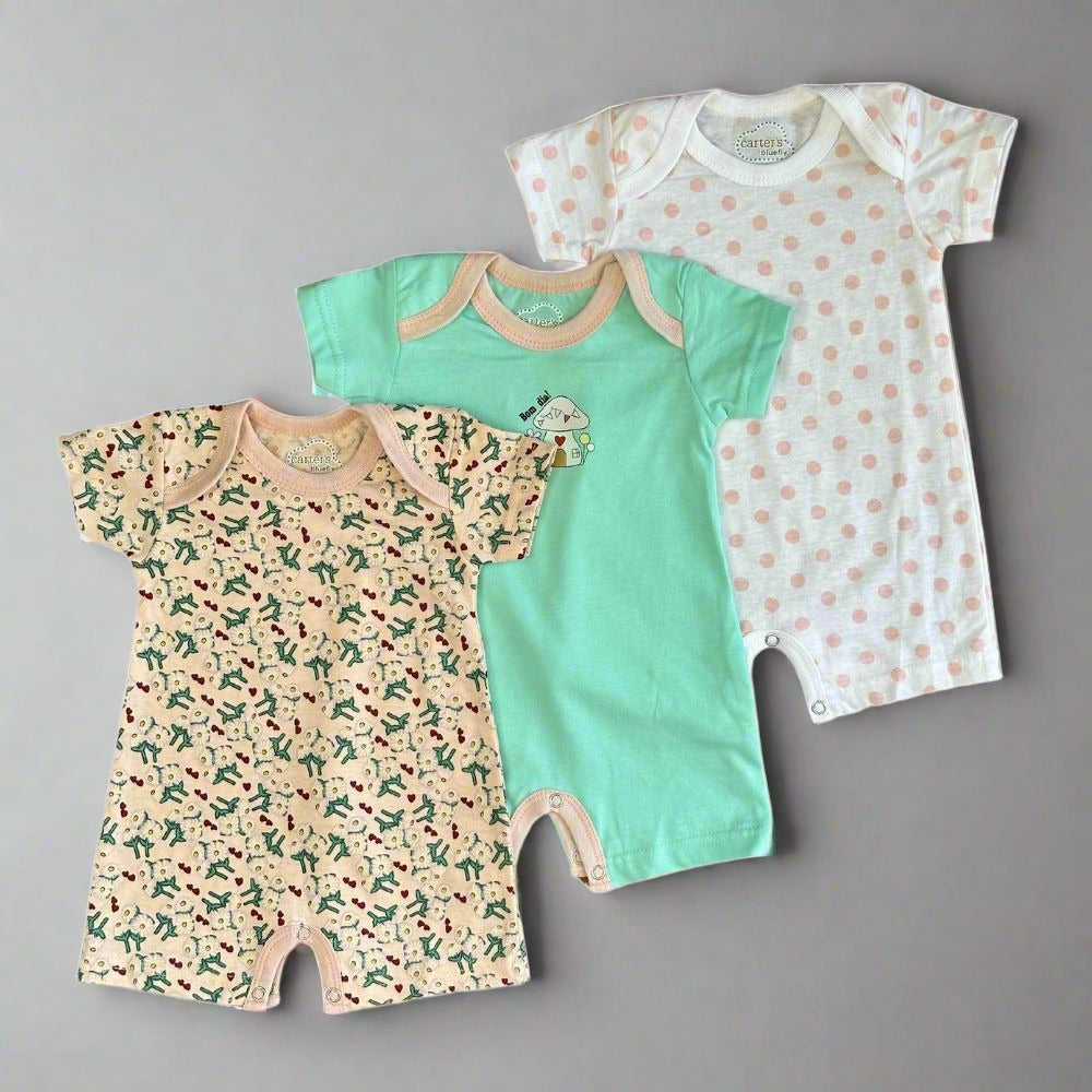 Three baby rompers from Alaya Junior's Carter's Exclusive 3-Pack are displayed on a gray background: the first is beige with dinosaurs, the second is mint green with a small dino, and the third is white with peach polka dotsβall in ultra-soft cotton.