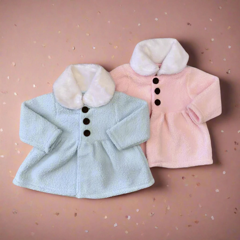 Two infant Alaya Junior Sherpa winter cardigans from the Baby Girl collection are displayed on a textured background. The left cardigan is pastel blue while the right is pale pink. Both have a soft, fluffy faux fur collar and dark brown buttons, designed to keep babies warm and cozy.