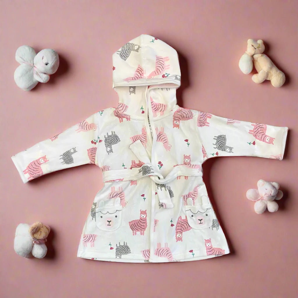 The Pink Cartoon-Themed Baby Bathrobe by Alaya Junior is displayed on a pink background, paired with plush toys: a bear, rabbit, butterfly, and sheep. Made in Thailand from machine washable fabric, it promises comfort for your little one.