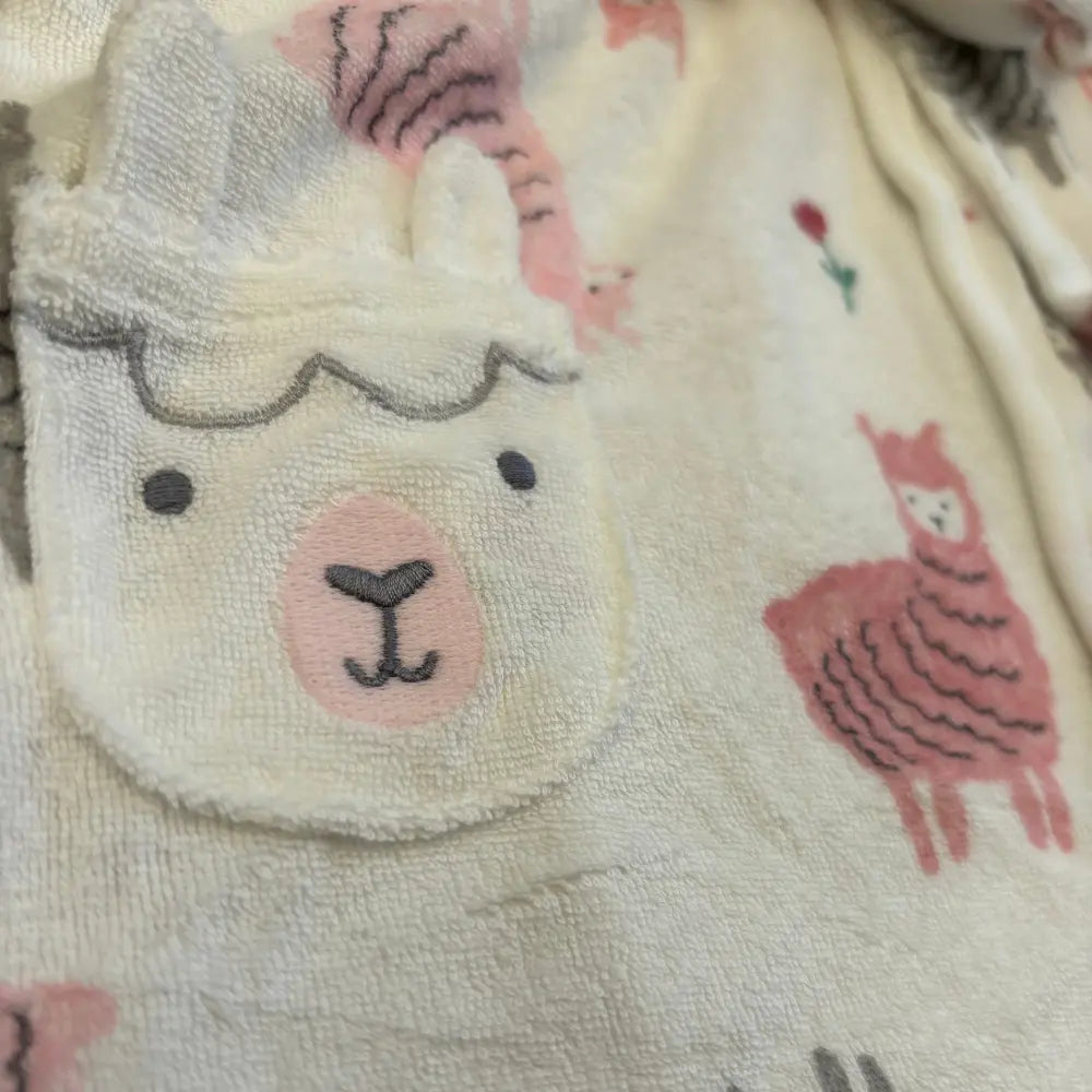Close-up of Alaya Junior's Pink Cartoon-Themed Baby Bathrobe, featuring a plush, cozy texture and washable fabric with pastel smiling llamas and other charming designs, plus a single red flower. Made in Thailand.
