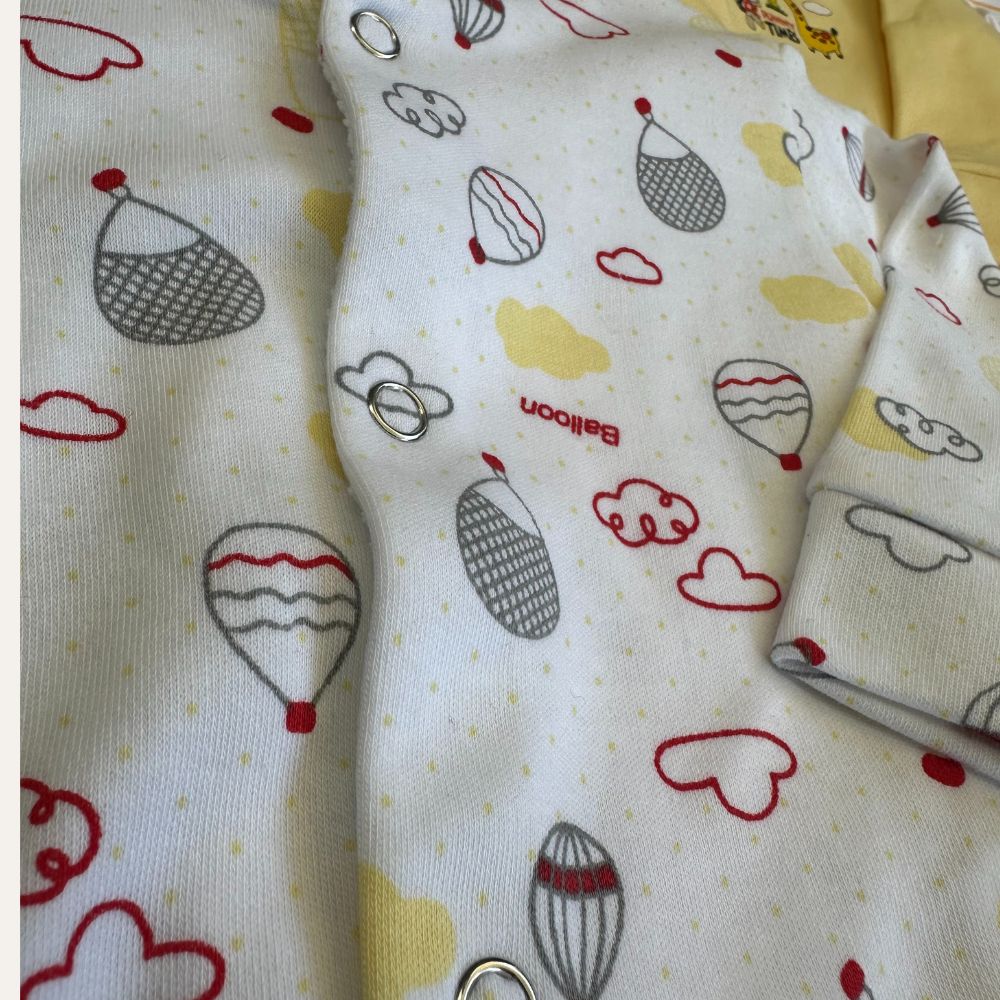 Close-up of a romper from Carter's Summer Baby Boy/Girl Pack of 3 Rompers (Set of Yellow), adorned with colorful prints of hot air balloons, clouds, and tiny dots. The fabric showcases a mix of red, grey, and yellow illustrations. This adorable piece of baby clothing features snap buttons along the front opening.