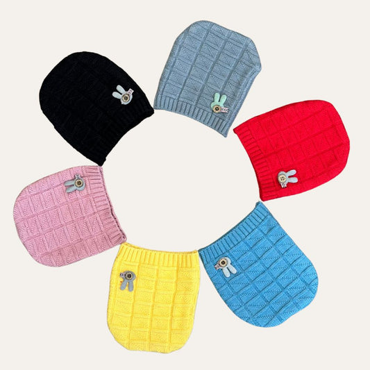 Six vibrant Cozy Cuddle knit hats by Alaya Junior are arranged in a circle on a light background. The hats come in black, gray, red, pink, yellow, and blue, each adorned with a delightful small animal patch on the side. These caps make an ideal addition to a baby's wardrobe as a gift of warmth with their prominently patterned grid design.