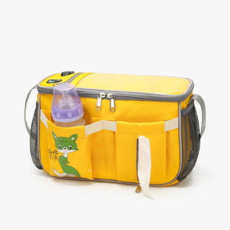 The Alaya Junior Diaper Bag + Stroller Organizer with Charging Cable is a multi-functional travel solution featuring gray handles, mesh side pockets, and vivid color options. This water-repellent yellow bag boasts an insulated main compartment with a zipper and multiple pockets - one pocket holds a purple baby bottle while another showcases a green cartoon fox.