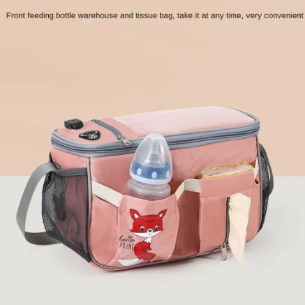 Introducing the Alaya Junior Diaper Bag + Stroller Organizer with Charging Cable β a multi-functional travel solution available in vibrant colors and adorned with a charming cartoon fox design. This pink diaper bag comes with handy external pockets, including one for a baby bottle and another featuring a tissue dispenser slot. Crafted from water-repellent material, it includes a grey zipper and adjustable shoulder strap, along with stylish text above the image.