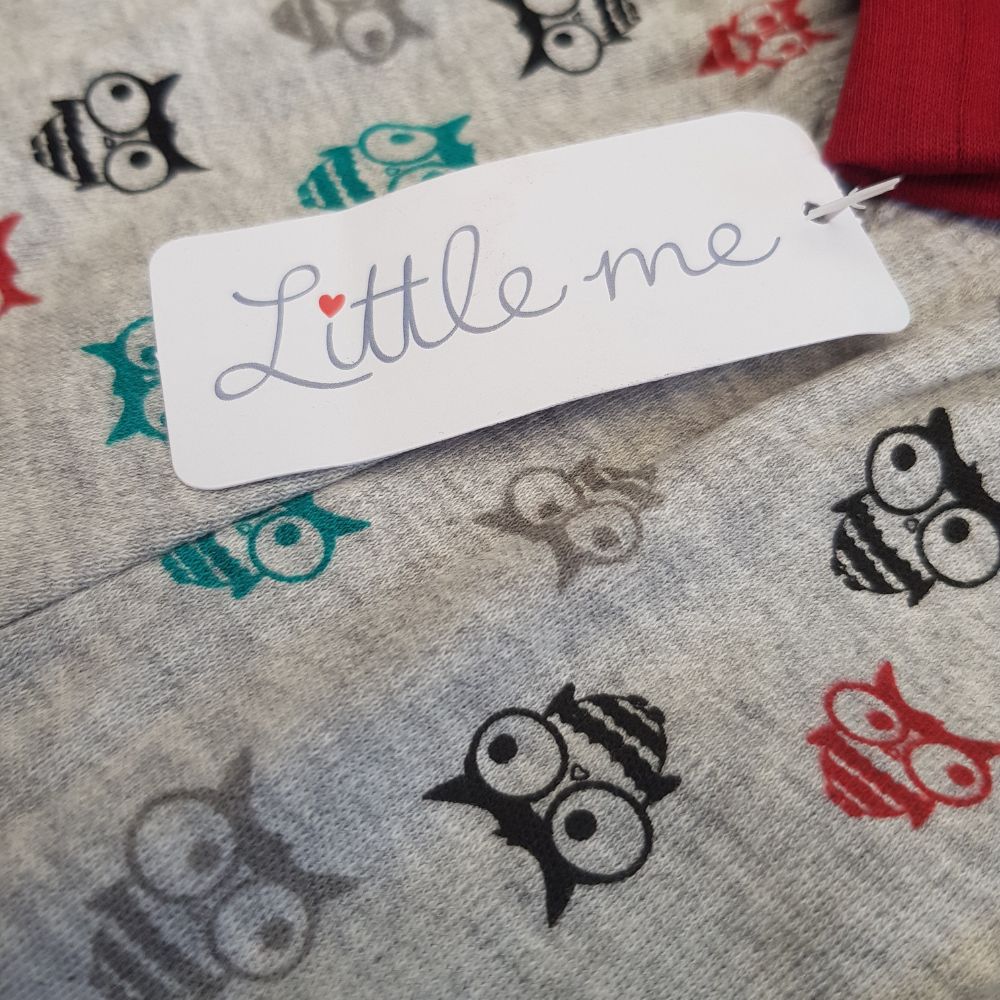 Close-up of a tag that reads "Little me" attached to the Little Me Happy Howl 2-Piece Winter Set for Babies from Alaya Junior. The fabric is light gray with a pattern of small, stylized owls in black, red, teal, and gray. The top edge of the clothing appears to be red. Ideal infant clothing from Pakistan for your little one.