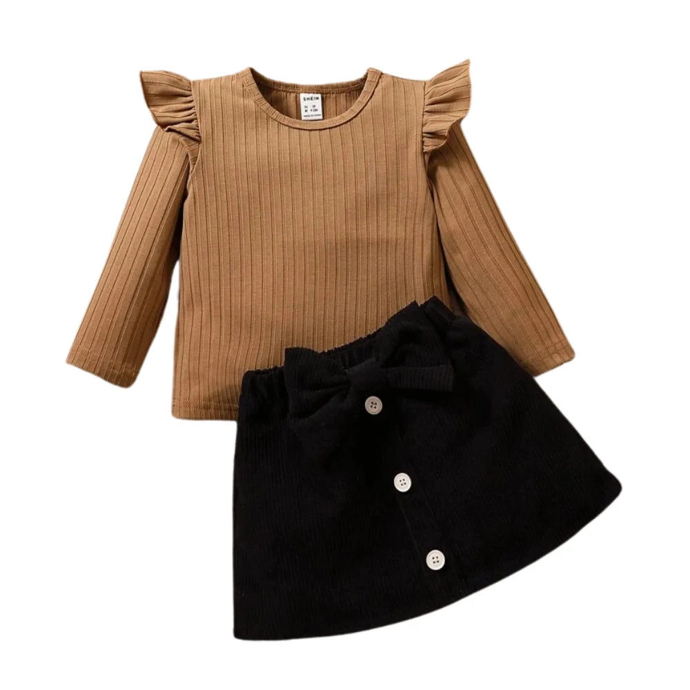 The SHEIN Baby Girl Ruffle Trim Tee, featuring beige ribbed fabric and chic ruffled shoulders, is paired with a black bow front skirt with a button-front design, elegantly displayed on a white background.