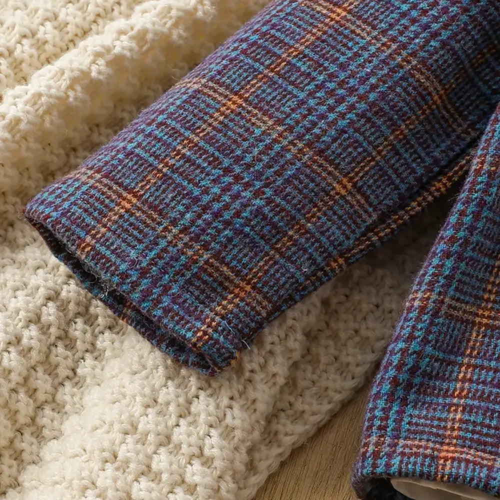 Close-up of two fabrics: a knitted cream textile with a textured look and plaid fabric in blue, brown, and orange hues reminiscent of the SHEIN Baby Boy Plaid Print Lapel Neck Blazer & Pants set. Both fabrics partially overlap on wood, evoking premium kids' clothing style.