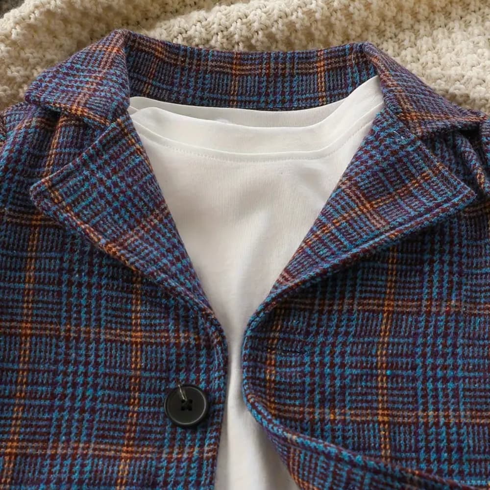 A SHEIN Baby Boy Plaid Print Lapel Neck Blazer in blue, brown, and black over a white tee. A single black button is visible on the textured beige surface. Perfect for stylish occasions with a comfortable fit.