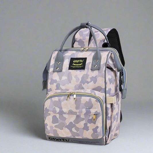 The Versatile Mom Backpack by Alaya Junior, featuring a waterproof gray and beige camouflage design, comes equipped with a front zipper pocket, top handles, and adjustable shoulder straps. This multifunctional diaper bag prioritizes convenience with its logo patch set against a plain gray background.