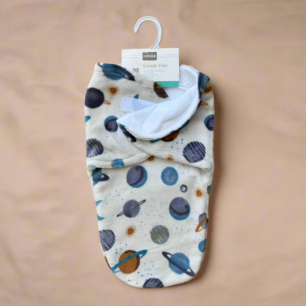 Introducing the Cozy Winter Swaddle with Planets Design by Alaya Junior. This charming baby wrap features an enchanting space-themed pattern of planets and stars. It is cream-colored, accented with blue, gray, and orange hues, and beautifully displayed against a beige background on a white hanger. Ideal for keeping your baby snug this winter season.