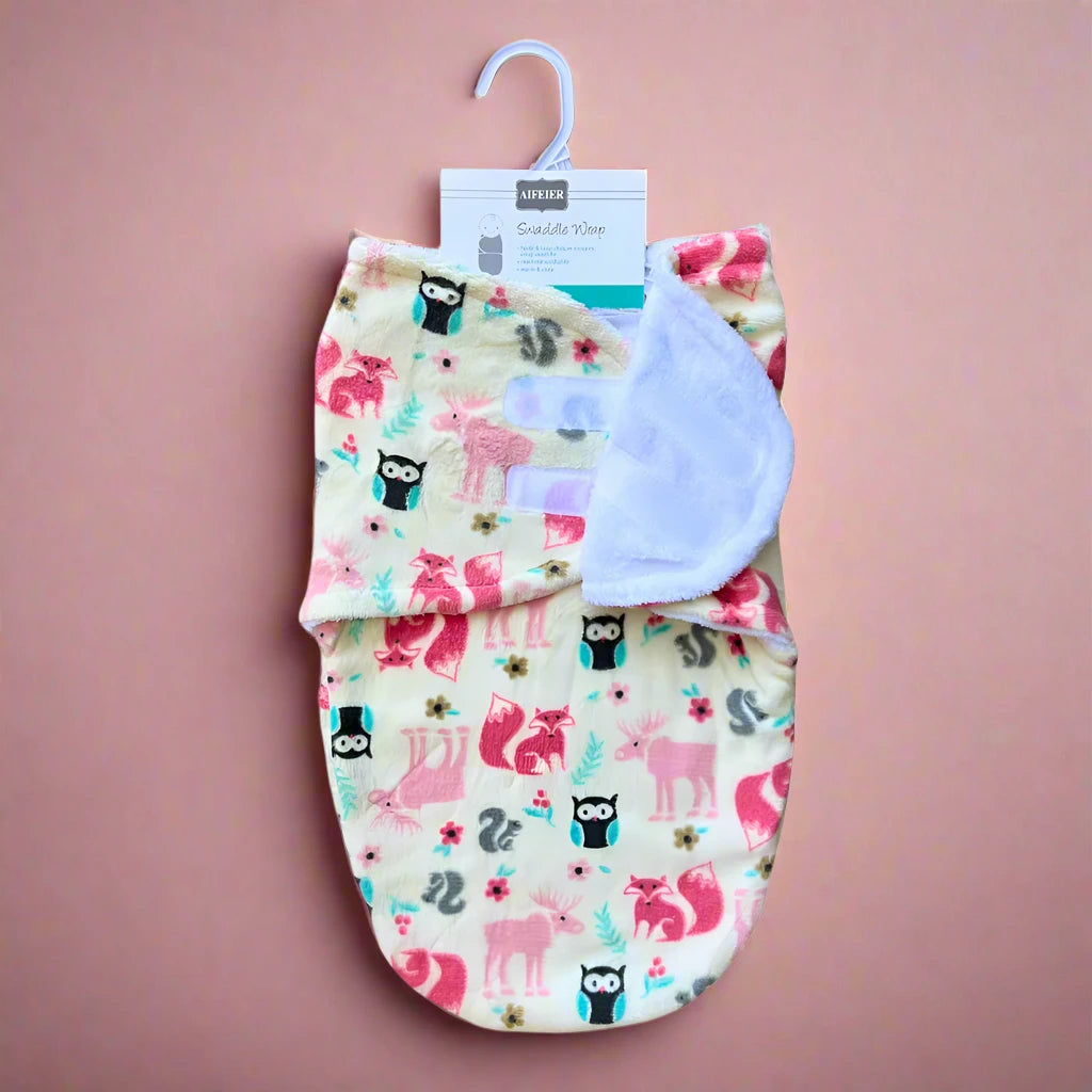 This charming and snug Baby Girl Pink Winter Swaddle by Alaya Junior features an enchanting woodland animal design, adorned with multicolored owls, foxes, and squirrels on a beige background. The blanket is attractively presented with a white hook atop a peach-colored surface.