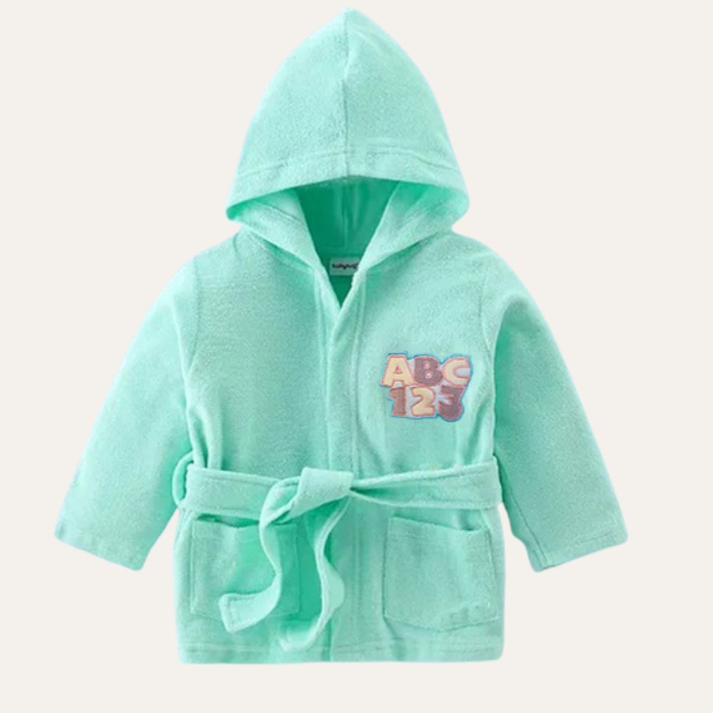 The Alaya Junior Cotton Baby Bathrobe with Hood is a light green robe featuring a front tie belt and two front pockets, designed for newborn babies. This cozy robe is adorned with an "ABC 123" graphic in purple, orange, and blue on the chest, making it an ideal piece of infant clothing in Pakistan that ensures both comfort and style.