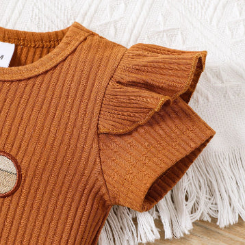 Close-up of the PATPAT Baby Girl Outfit Set featuring a rust-colored summer romper with ruffled short sleeves, displayed on a fringed white blanket. A small plaid patch adorns the front, enhancing the charm of this adorable dress from PATPAT.