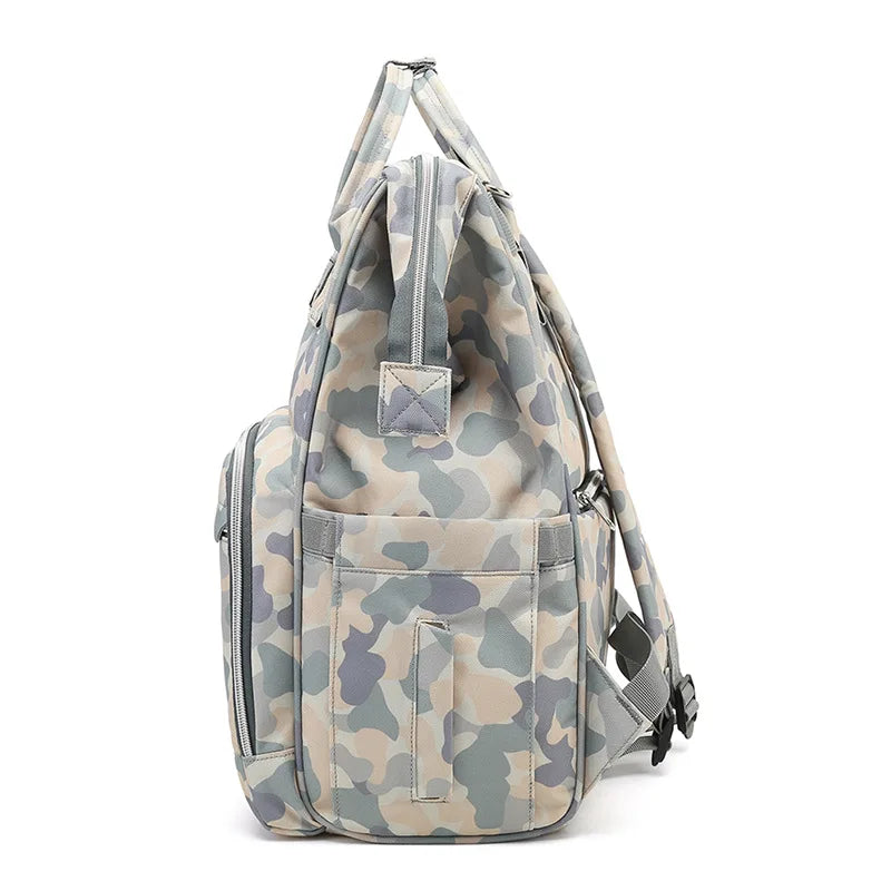 A side view of the Versatile Mom Backpack: Waterproof Camo Diaper Bag by Alaya Junior showcases a practical gray and beige camouflage pattern, with multiple compartments and adjustable shoulder straps, making it perfect for everyday use.