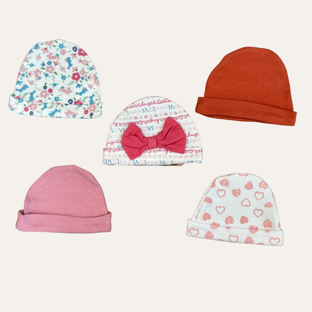 An assortment of five baby hats on a plain background, perfect for newborns. These hats feature diverse designs and colors: one with a floral print, one with alphabet script and a bow, one solid red, one solid pink, and one with a heart pattern. Ideal infant clothing from Pakistan. Introducing the "Organic Delight: 5-Pack Soft Cotton Printed Caps for Baby Girl (0-9 Months)" by Alaya Junior.