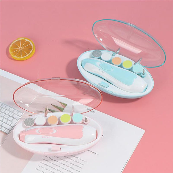 Two Electric Baby Nail Trimmers with 6 Grinding Heads by Alaya Junior are displayed on a pink surface in open cases. One kit features a blue case, and the other has a pink case. Each trimmer comes with various attachments, including buffing heads and files. A keyboard, a lemon slice, and some baby clothing from Pakistan are also visible.
