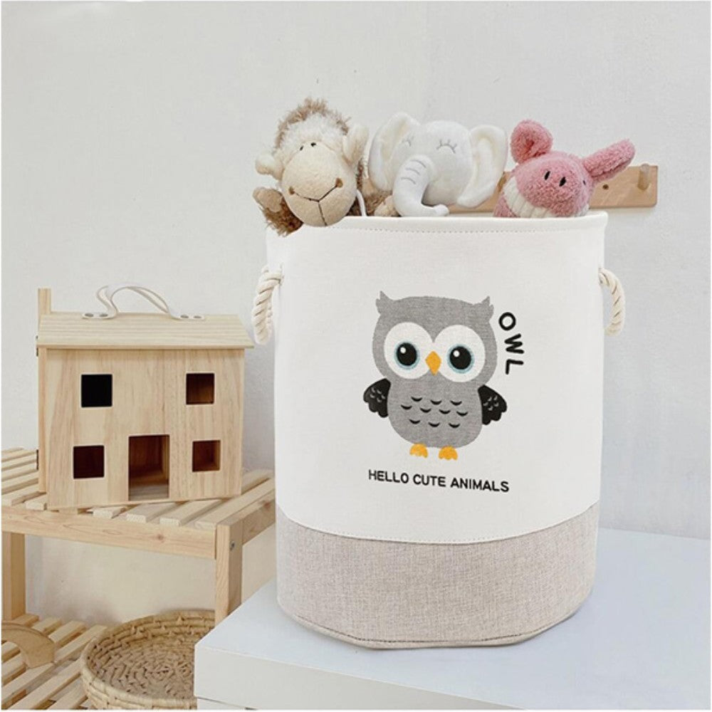 The SHEIN Kids Large Folding Laundry Basket, featuring a cute owl design and "Hello Cute Animals," holds plush toys like a sheep, elephant, and piglet. It is placed next to a wooden toy house on a wooden shelf.