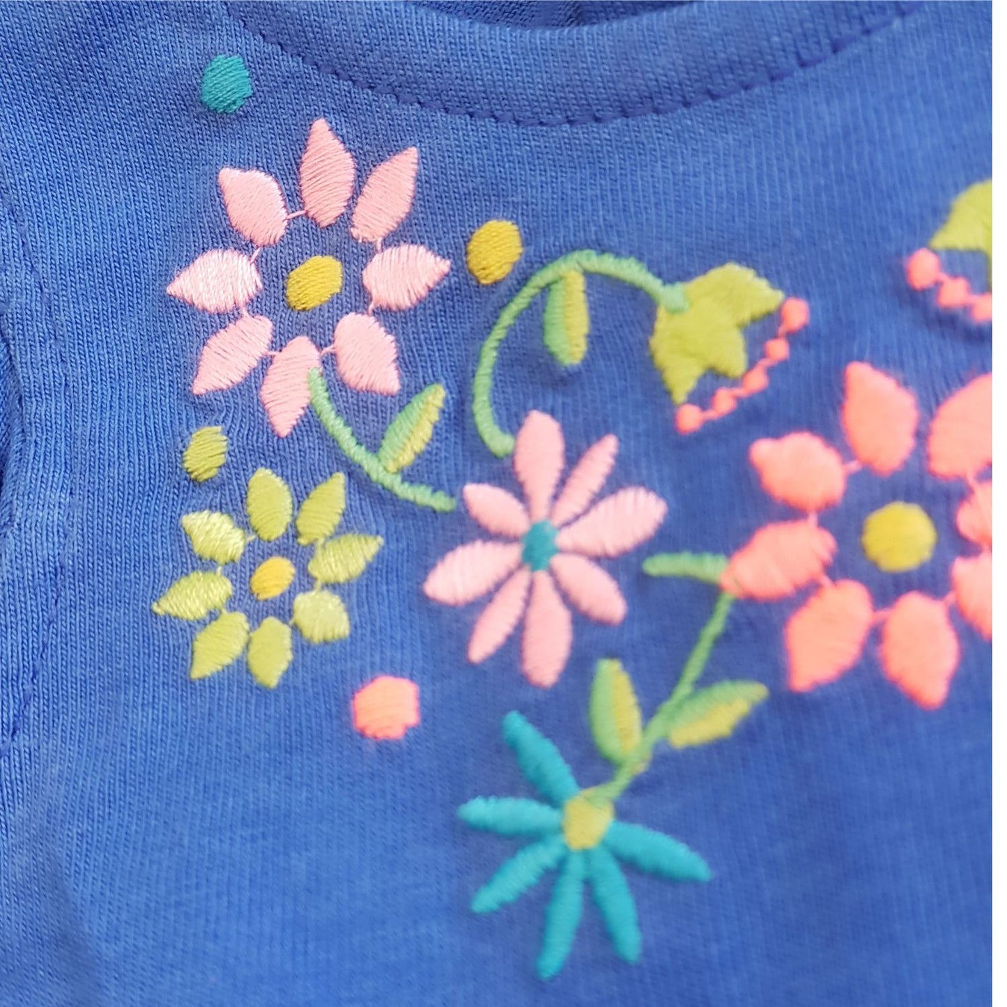 Close-up of embroidered pink, yellow, and green flowers on blue fabric. The embroidery showcases detailed floral patterns with various flower shapes and leaves, adding a colorful and decorative touch to this Baby Girls Embroidered Jumpsuit from Thailand by Alaya Junior.