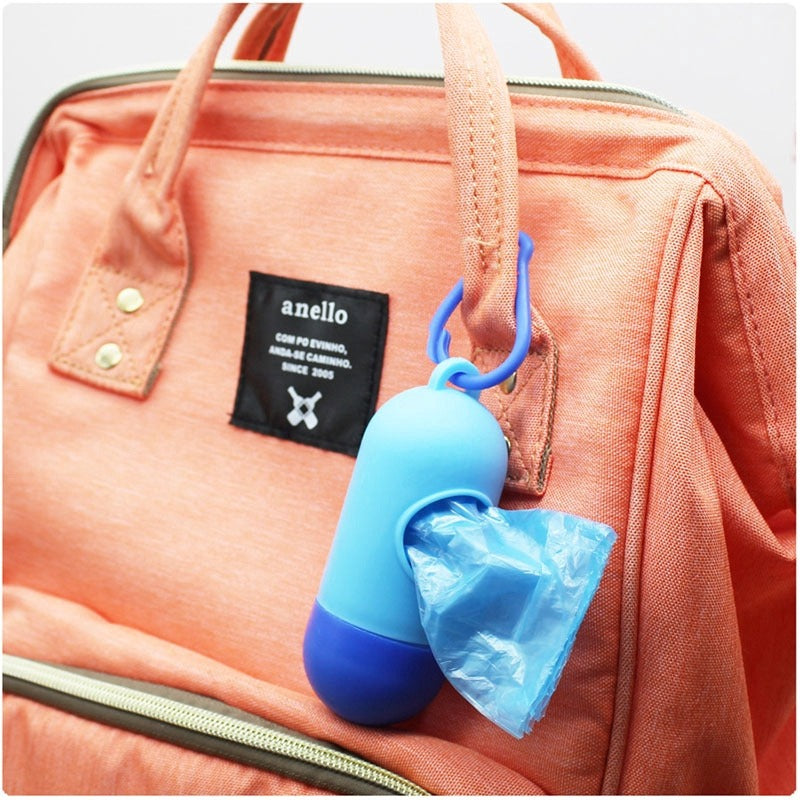 A coral backpack features an Alaya Junior's blue capsule-shaped bag dispenser attached to a strap, containing 4 rolls of odor-resistant, biodegradable plastic bags ideal for diaper waste.