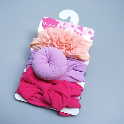 Introducing the Baby Girls' Adorable Trio Three-Piece Headband Set by Alaya Junior: a charming collection designed to enhance baby girl fashion. This delightful set, elegantly presented on a card, features three essential hair accessories for any stylish little one—a peach band adorned with a flower, a lavender band with a soft round knot, and a pink band showcasing a large bow.