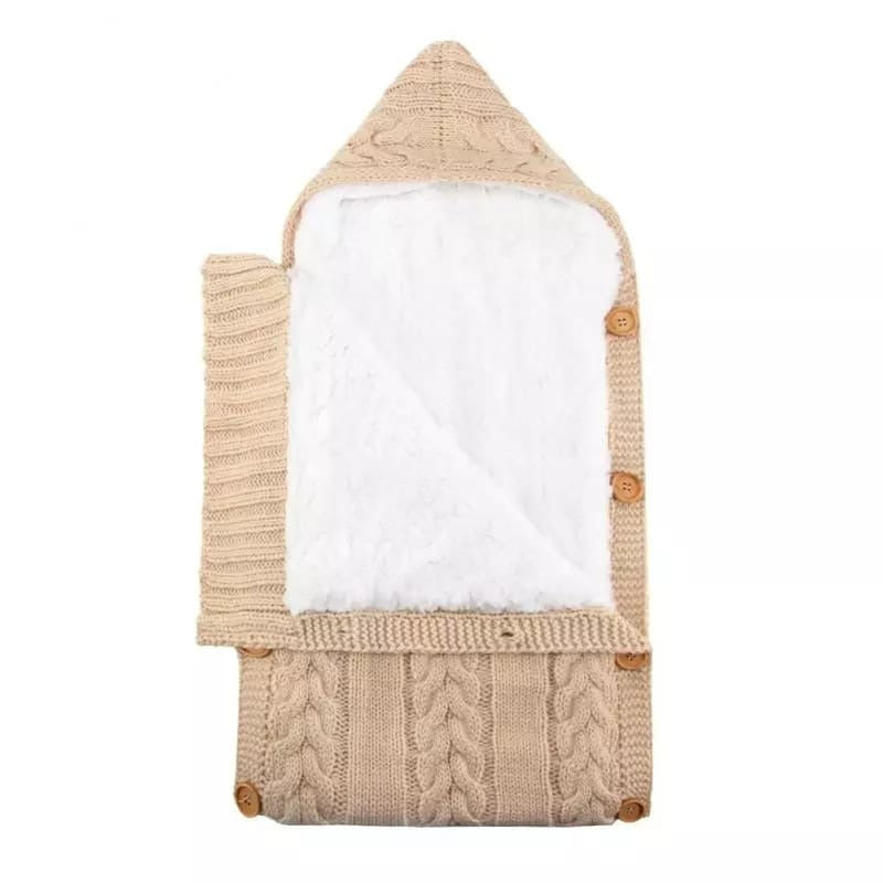 Introducing the Alaya Junior Newborn Baby Sleeping Bag with Sherpa Lining for ages 0-7 months: a beige, knitted fabric wrap featuring a cozy white fleece-lined interior. It boasts a stylish cable knit design and convenient wooden side buttons for fastening. Displayed open and laid flat, the interior reveals adjustable Velcro closures for added comfort and security.