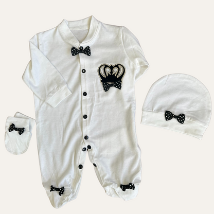 Experience adorable elegance with Alaya Junior's Charming Trio: MJ Baby Bow Romper Set. This white ensemble features a romper with black polka dot bows, a swan emblem, footed legs with charming bow accents, and includes a matching hat and cozy mittens for the perfect blend of comfort and style.