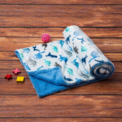 A soft, rolled-up Luvable Friends' Dino Delight: Unisex Sherpa-Backed Plush Blanket by Alaya Junior featuring a Dino Dreamland print lies on a wooden surface. The ultra-plush front is primarily blue and white, adorned with colorful dinosaur shapes. Nearby are small toys: a pink woven ball and red, blue, and yellow wooden block shapes.