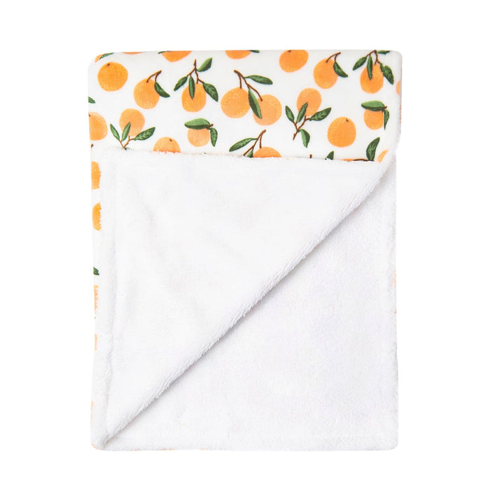 The Alaya Junior Luvable Friends' Citrus Bliss: Unisex Sherpa-Backed Plush Blanket is displayed with a corner folded over, showing the underside. The top side features a citrus motif with orange fruit and green leaves on white fabric, while the plush underside reveals an ultra-plush texture for added comfort.