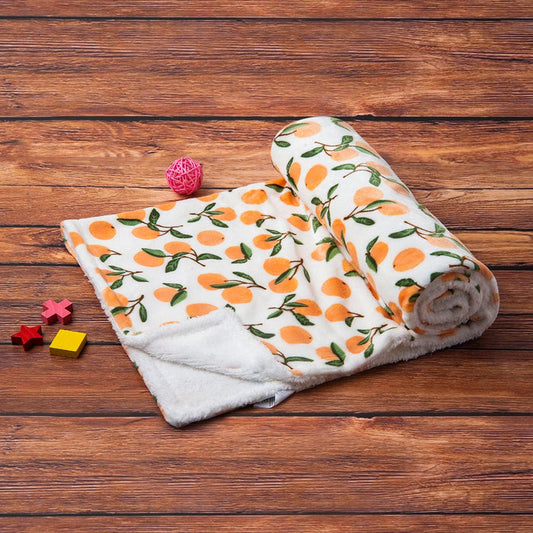 A soft, white Alaya Junior Luvable Friends' Citrus Bliss: Unisex Sherpa-Backed Plush Blanket, featuring an orange and green fruit pattern, is partially unrolled on a wooden surface. Nearby are small wooden toys in red, yellow, and natural wood colors, along with a pink decorative ball—ideal for complementing any newborn baby's nursery.