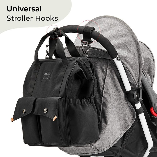 The Ellie & Luke Multifunctional Diaper Bag (Black) by Ellie And Luke, featuring a modern design, is attached to a gray stroller's handlebar with universal hooks. It offers multiple compartments, insulated bottle holders, and silver clasps for ample storage and on-the-go convenience.