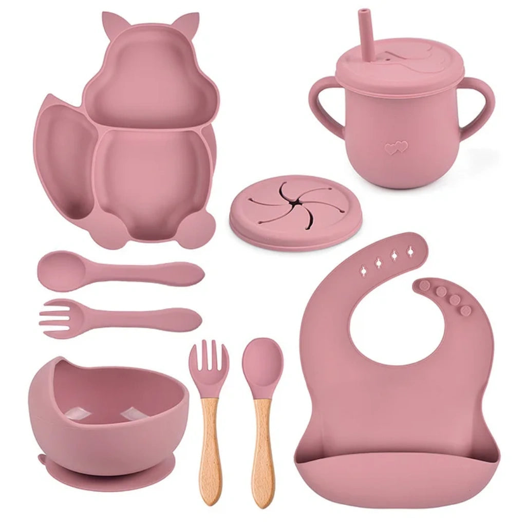 Pink children's dining set including bowl, spoon, fork, cup, and bib on a white background