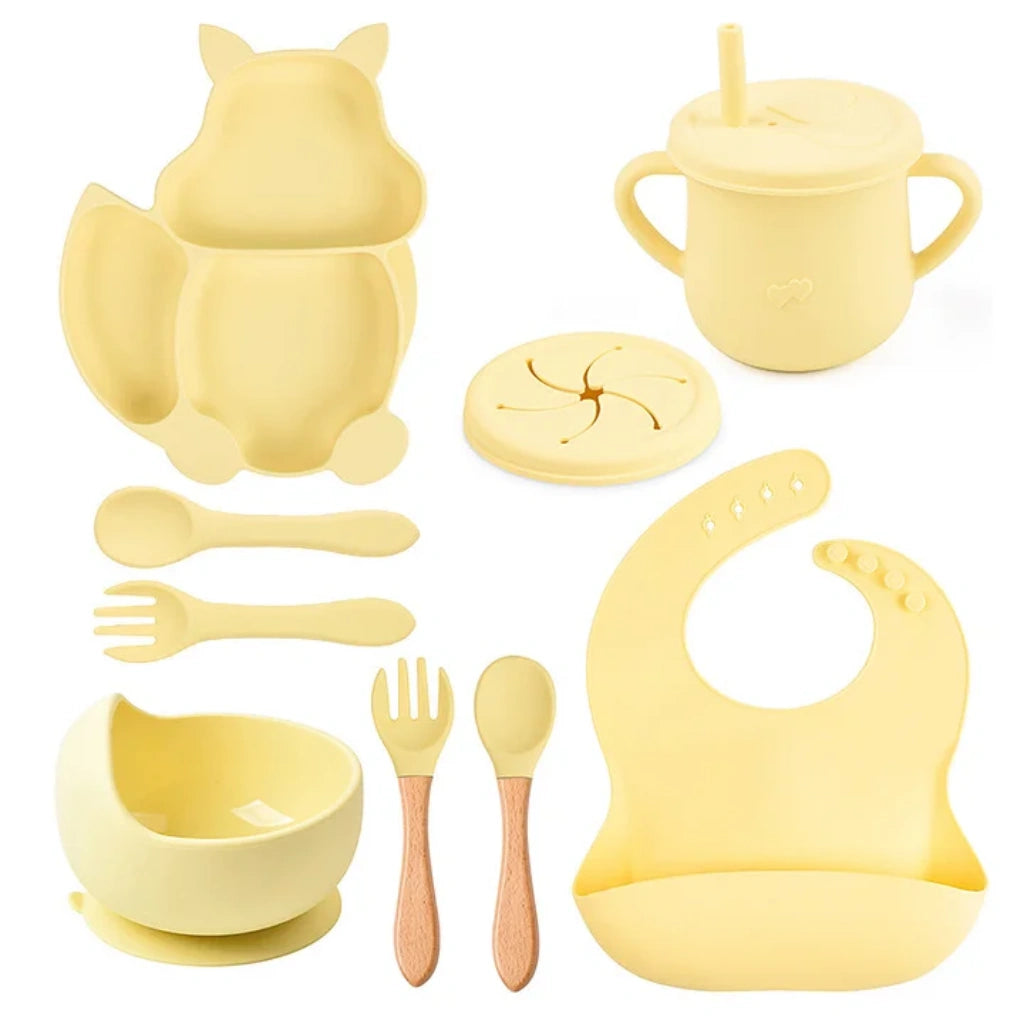 Yellow baby feeding set including cup, bowl, spoon, and bib on a white background