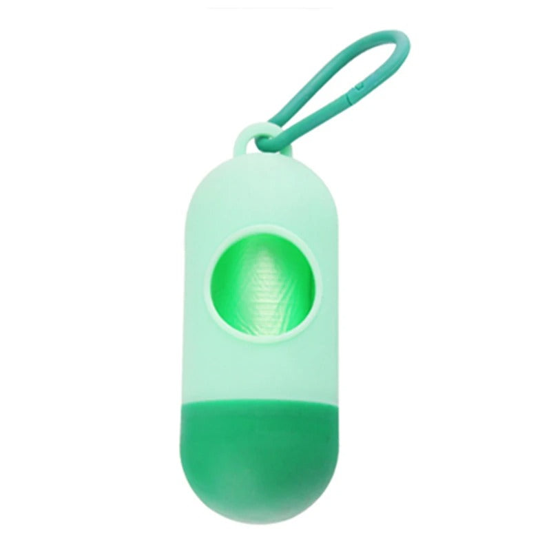 A compact, green, capsule-shaped container with an odor-resistant carabiner clip, featuring a circular opening housing a roll of Alaya Junior's biodegradable plastic bags for diaper waste disposal.