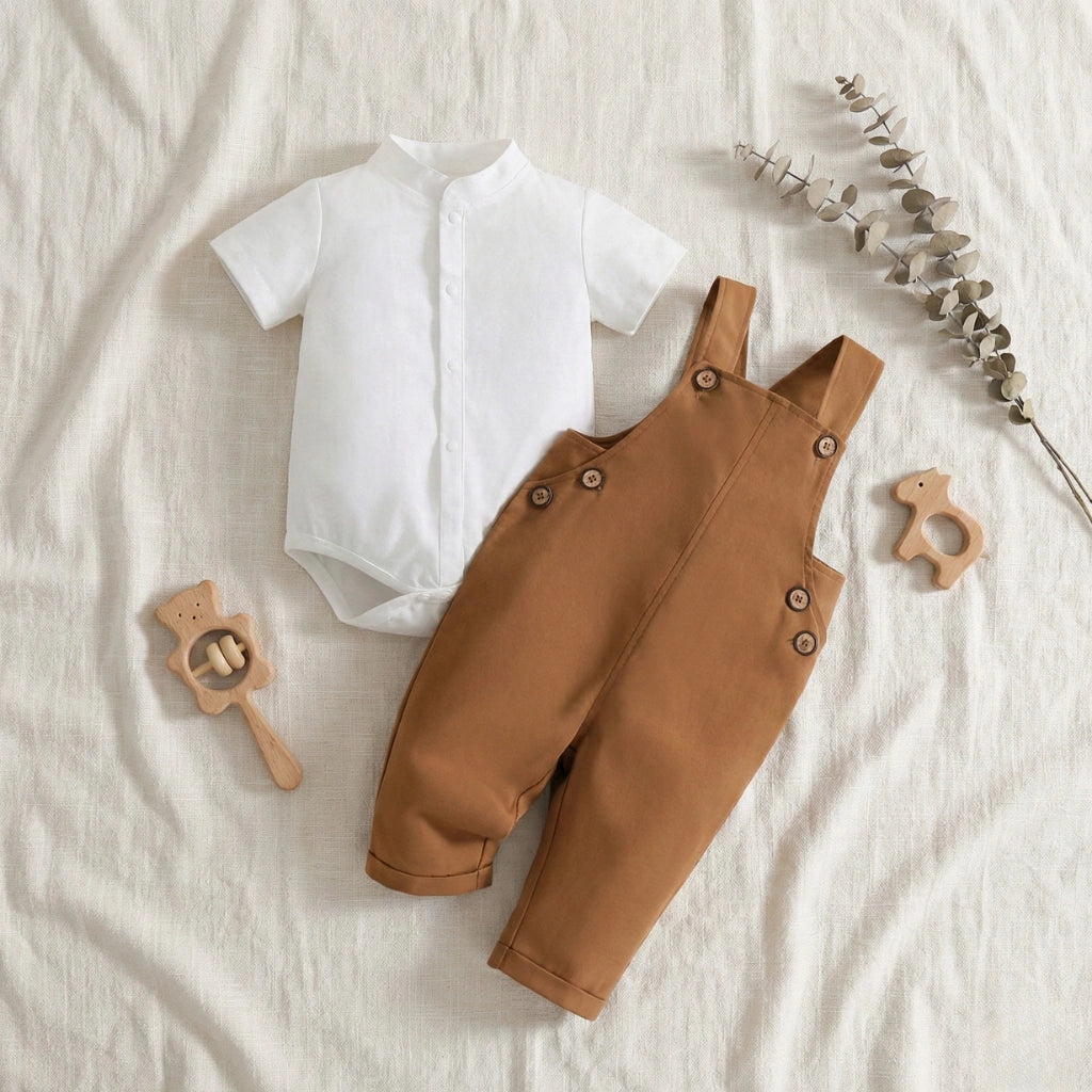 White baby shirt and brown overalls on a light background with wooden toys.