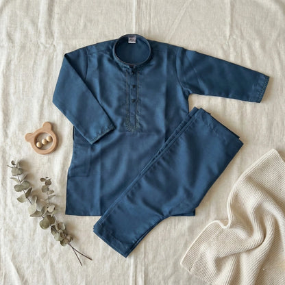 Blue children's outfit with long-sleeve shirt and pants on a textured surface with decorative elements.