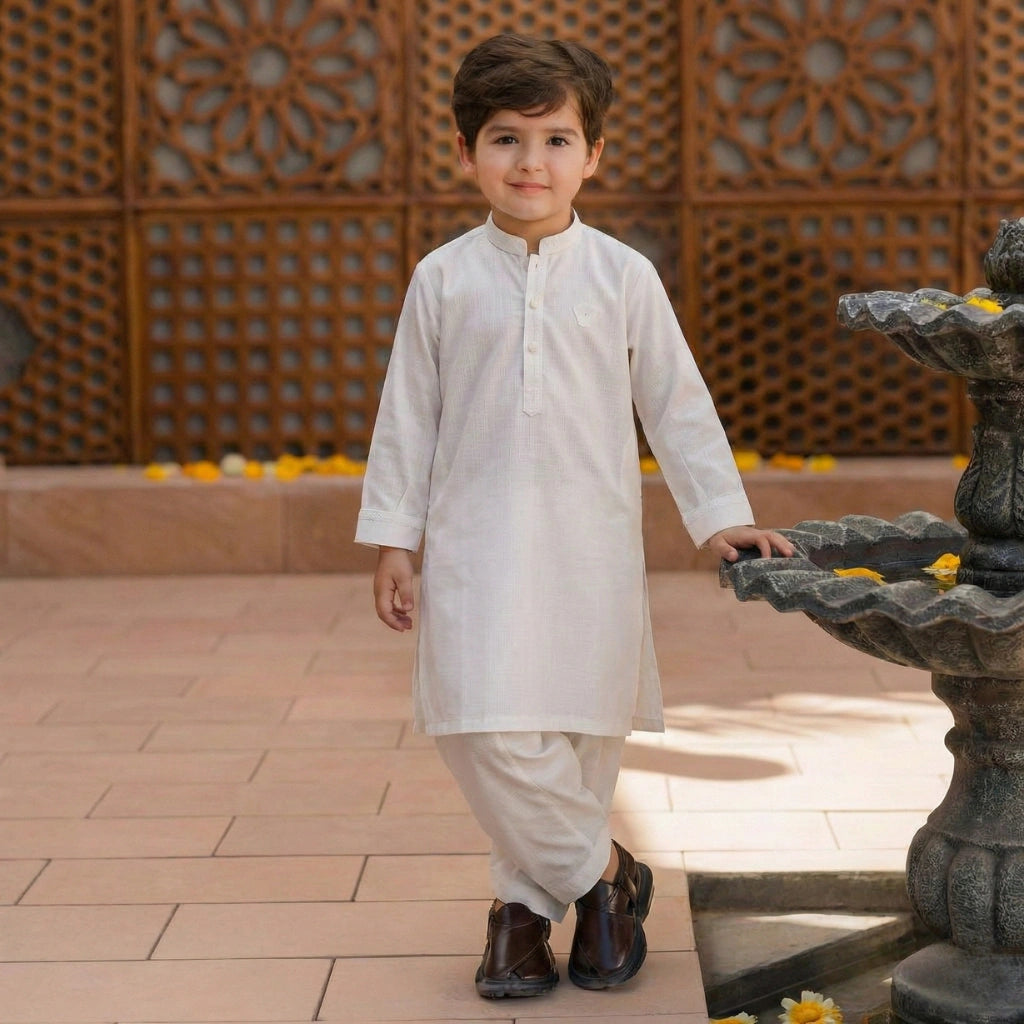 Child in traditional white outfit standing next to a decorative fountain with a patterned wall in the background.