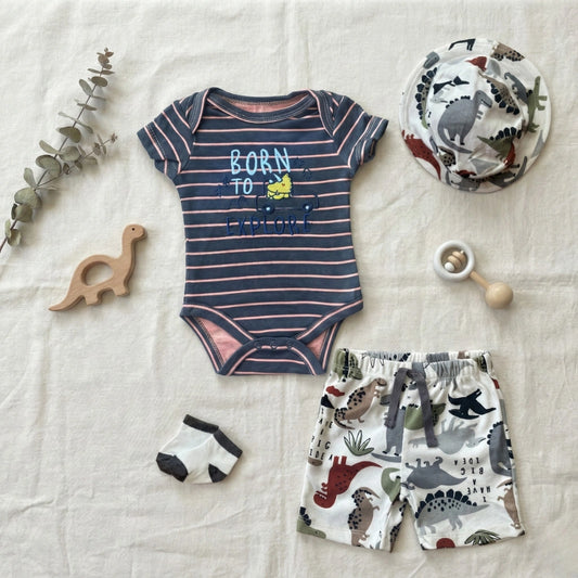 Baby clothing set with striped onesie, shorts, and accessories on a textured surface.