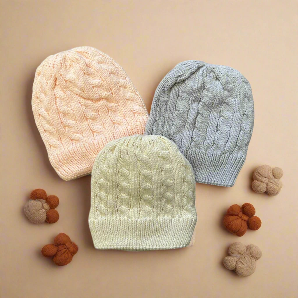Three knit baby hats in peach, green, and gray on a white background