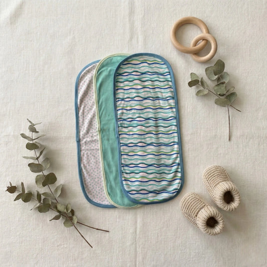 Baby items including a striped cushion, wooden ring, and knitted toys on a light background