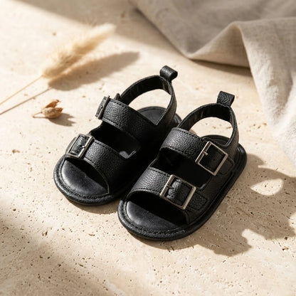 Pair of black sandals with buckles on a beige surface