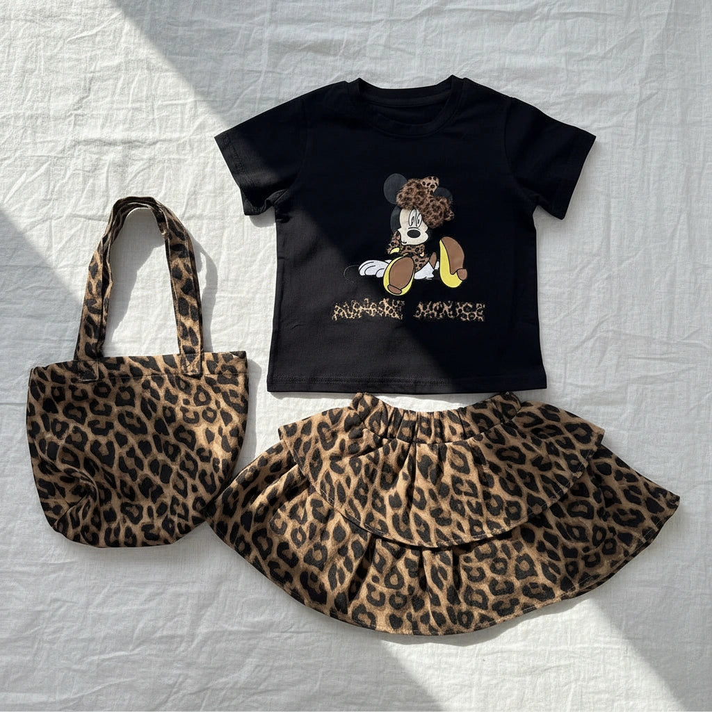 Black t-shirt with cartoon character, leopard print skirt, and tote bag on a textured white surface