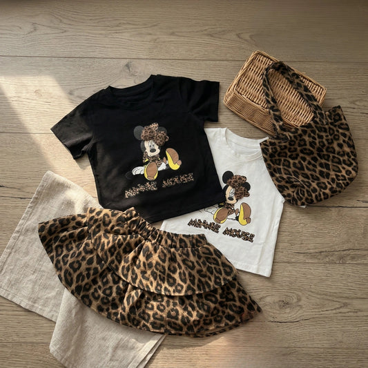 Black t-shirt with cartoon character, white t-shirt with cartoon character, leopard print skirt, and leopard print bag on a wooden surface.