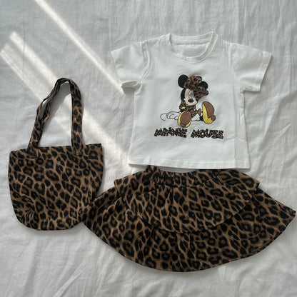 White t-shirt with cartoon character, leopard print skirt, and tote bag on a white background
