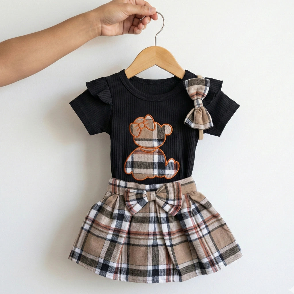 Children's outfit with black top and plaid skirt on a hanger against a white background