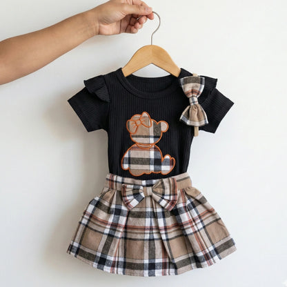Children's outfit with black top and plaid skirt on a hanger against a white background