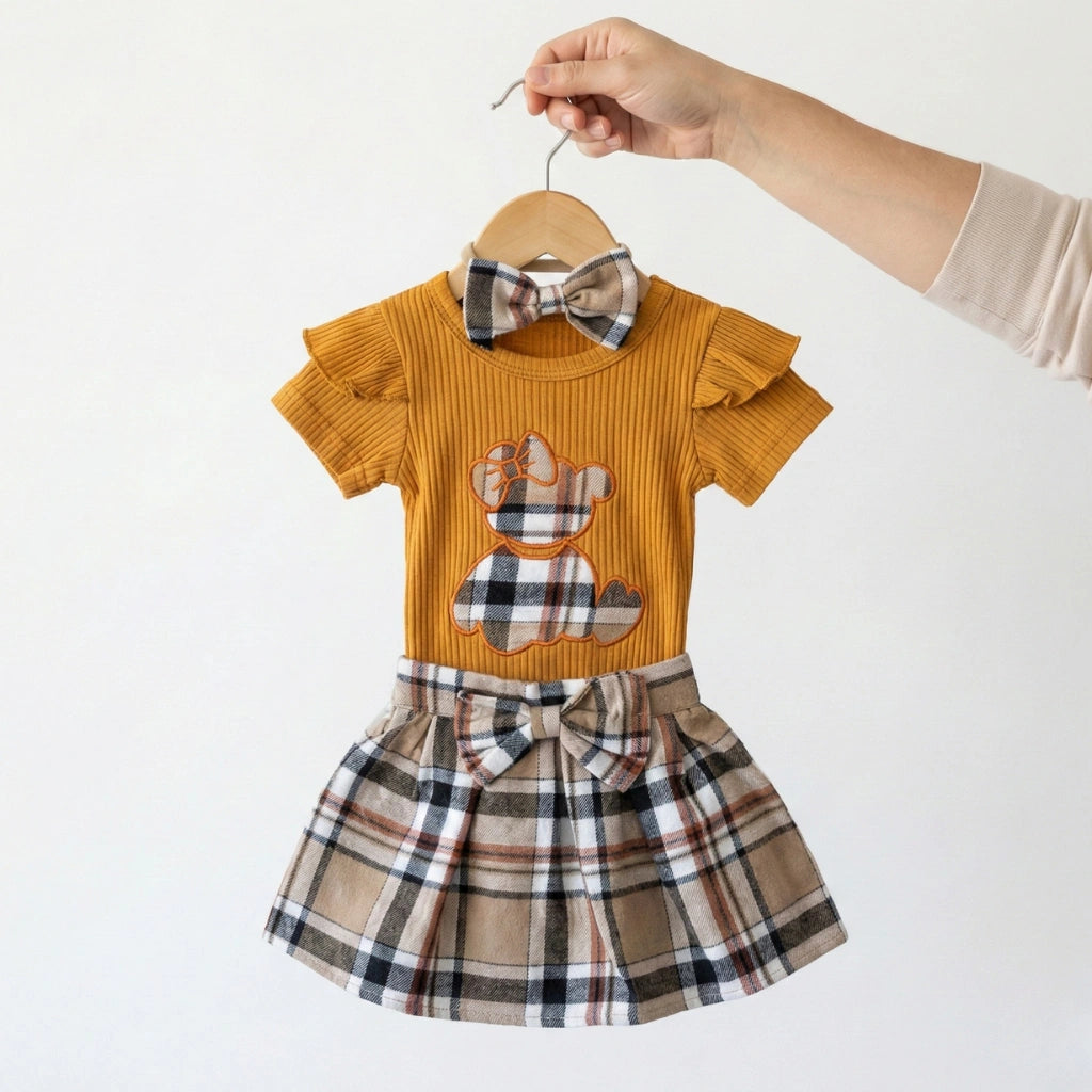 Children's outfit with mustard top and plaid skirt on a hanger against a white background