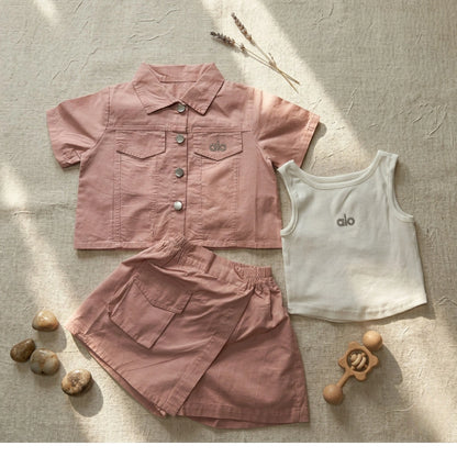 Children's pink shirt, white tank top, and pink shorts with 'alo' branding on a textured surface.